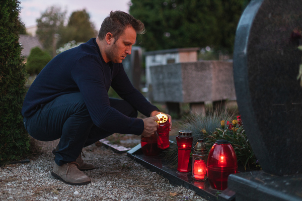 Mann zündet eine Kerze am Grab an. / iStock/Anze Kralj Mann zündet eine Kerze am Grab an.